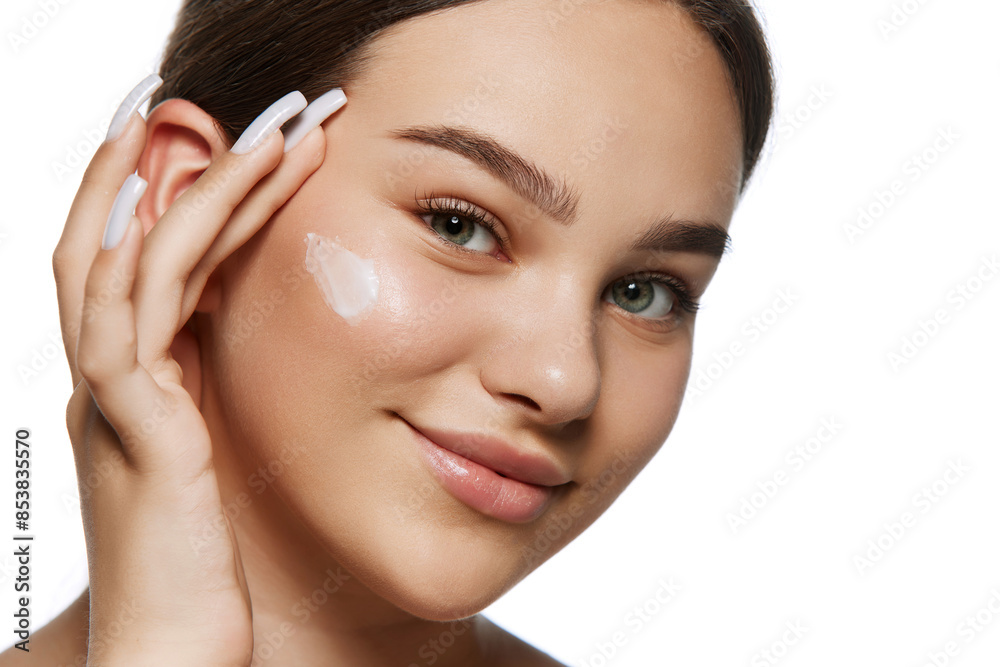 Close-up portrait of young woman with well-kept, health spotless skin, applying face moisturizing cream isolated on white background. Natural beauty, skincare, cosmetology, cosmetic products concept
