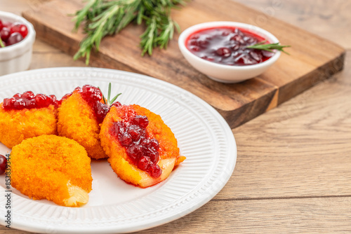 Baked or fried Camembert or brie cheese with cranberry and rosemary sauce on wooden Table