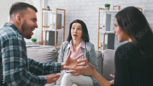 A couple is in the middle of a heated argument during a therapy session in an office setting. The woman in the middle is visibly distressed as she tries to calm the couple down. photo