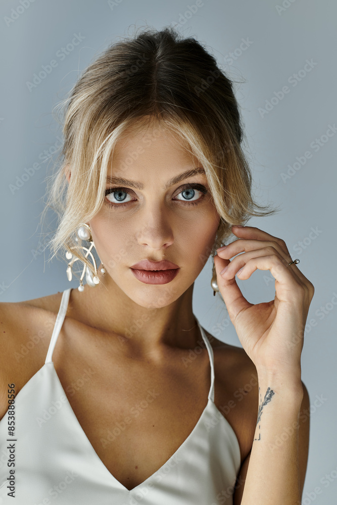 A young woman with blonde hair elegantly posing in a white top, exuding grace and beauty against a grey background. A young woman with blonde hair elegantly posing in a white top, exuding grace and beauty against a grey background.