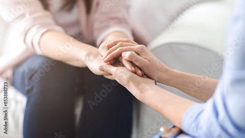 One woman offers comfort and reassurance by holding another woman hand during a heartfelt conversation in a cozy living room setting, cropped