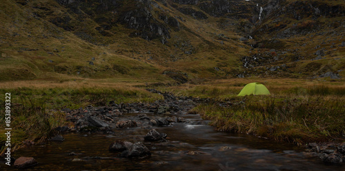 Panoramic view of a green camping tent next to a river in Corrie Fee, Cairngorms National Park of Scotland, with waterfall in background photo