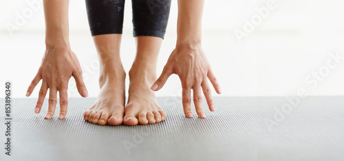 Fotografi Cropped of woman is seen performing a stretching exercise in a studio, with hands touching feet on a yoga mat