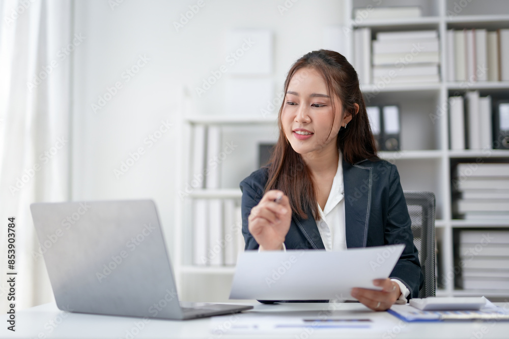 Young businesswoman working with documents at her desk in modern office, focused on analyzing paperwork with laptop open. Young businesswoman working with documents at her desk in modern office, focused on analyzing paperwork with laptop open.