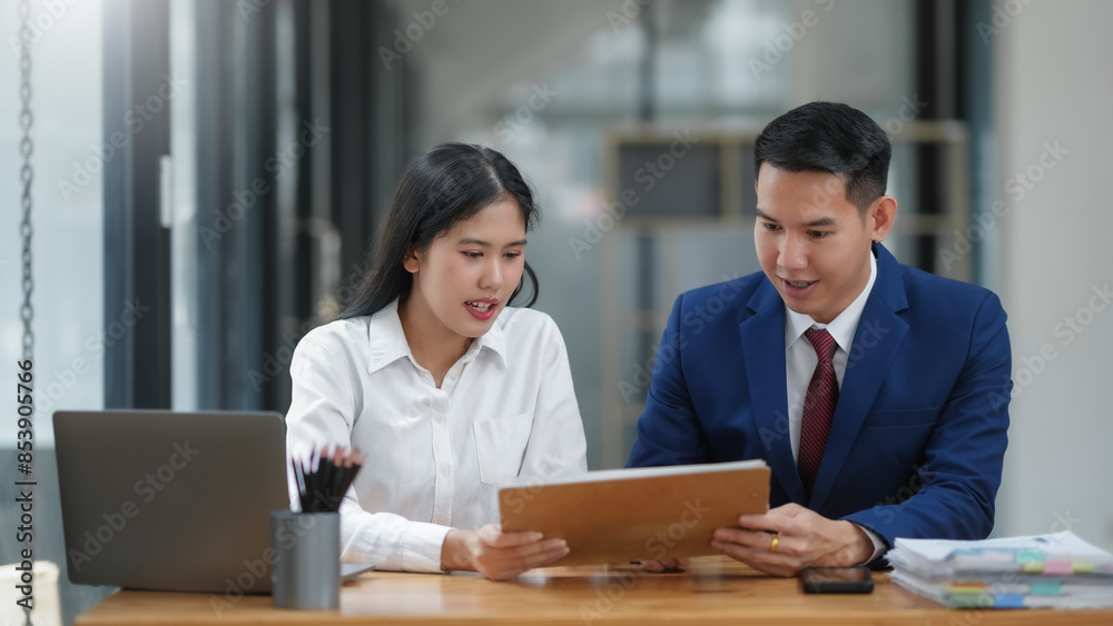 Two business professionals in a modern office discuss documents, exemplifying teamwork and collaboration. Two business professionals in a modern office discuss documents, exemplifying teamwork and collaboration.