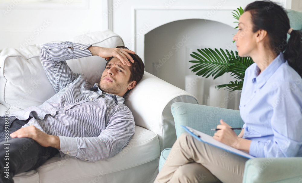 Frustrated man is seen discussing his thoughts with a therapist in a cozy living room. He appears distressed, resting his head on his hand, while the therapist listens attentively and takes notes. Frustrated man is seen discussing his thoughts with a therapist in a cozy living room. He appears distressed, resting his head on his hand, while the therapist listens attentively and takes notes.