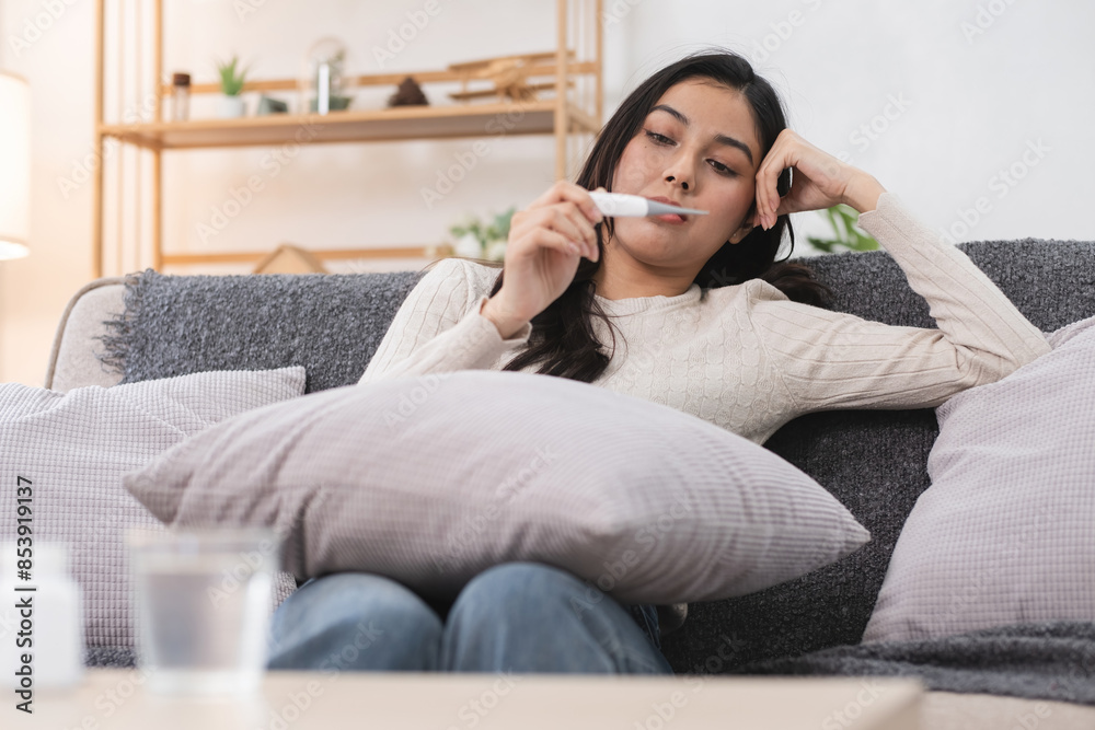 Young Woman Checking Temperature with Thermometer While Sitting on Couch at Home Young Woman Checking Temperature with Thermometer While Sitting on Couch at Home