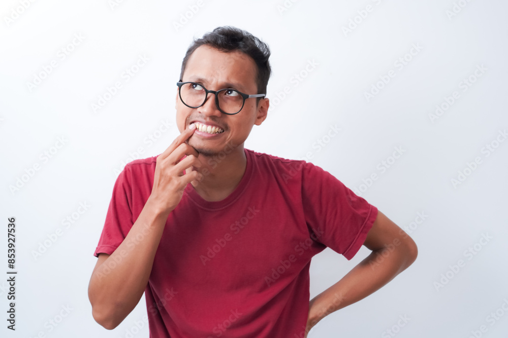 Young asian man posing thinking, looking up and putting index finger near teeth, wearing red t-shirt isolated on white background. Shot in studio. Young asian man posing thinking, looking up and putting index finger near teeth, wearing red t-shirt isolated on white background. Shot in studio.