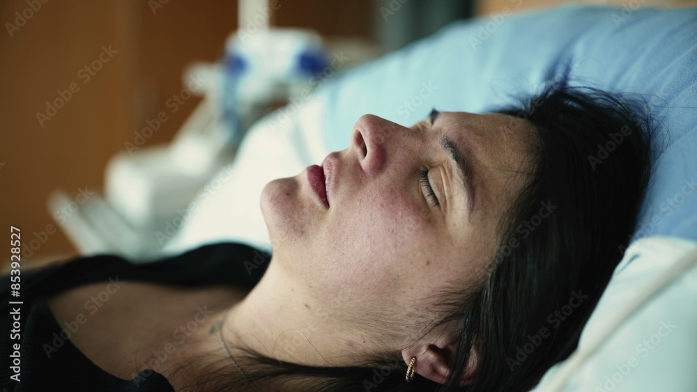 Close-up face of woman having physical pain while laid in hospital bed with eyes closed in discomfort Close-up face of woman having physical pain while laid in hospital bed with eyes closed in discomfort