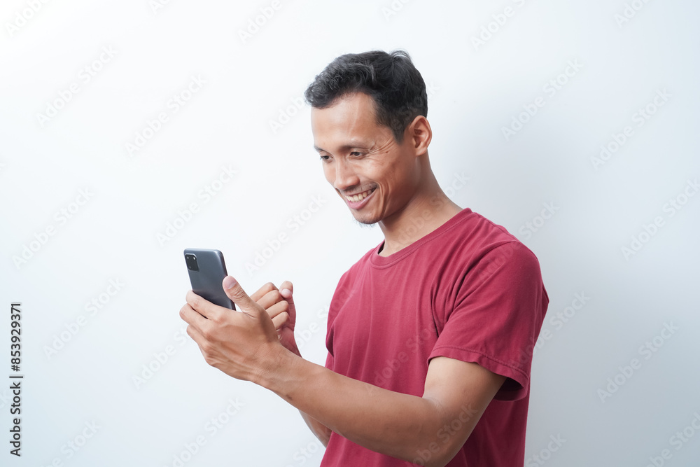a young man wearing a red t-shirt holding a cellphone is calling happy expression on an isolated white background a young man wearing a red t-shirt holding a cellphone is calling happy expression on an isolated white background