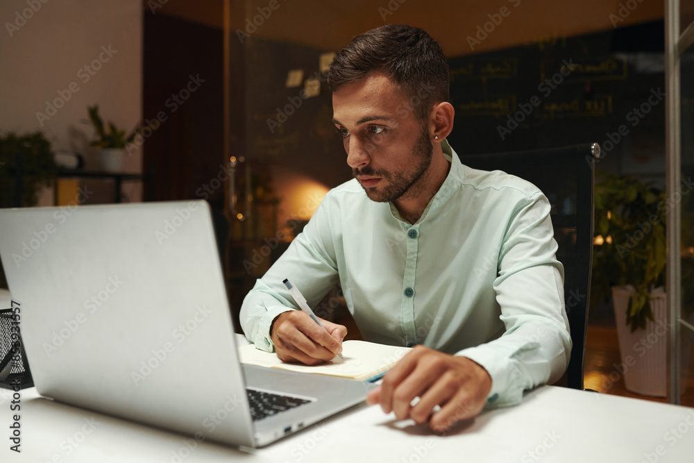 Developer reading article on laptop and taking notes