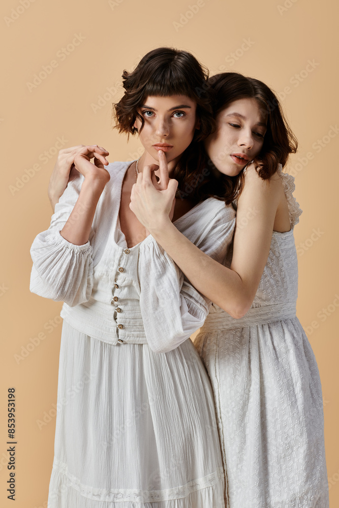 Two young women wearing white summer dresses embrace against a beige backdrop. Lesbian couple Two young women wearing white summer dresses embrace against a beige backdrop. Lesbian couple