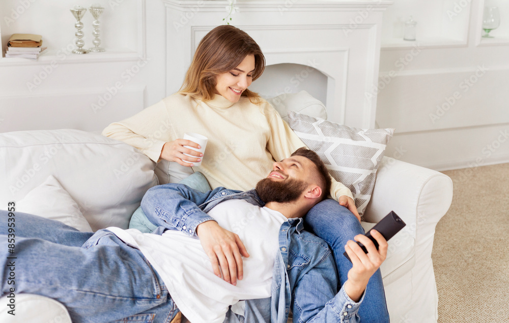 A man and a woman are seated together on a couch in a living room setting. A man and a woman are seated together on a couch in a living room setting.