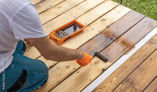 Wallpaper Mural A person wearing gloves applies wood stain to a wooden deck with a roller. A tray of stain sits beside the person on the deck. Torontodigital.ca