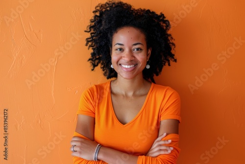 Portrait of a smiling afro-american woman in her 30s with arms crossed isolated on pastel orange background photo