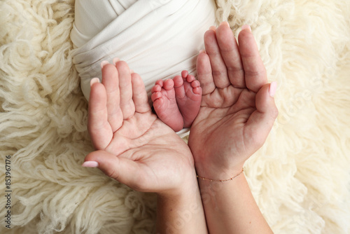 Feet of the newborn on the palms of the parents. The palms of the father and mother are holding the foot of the newborn baby in a white flokati blanket. Photography of a child's toes, heels and feet.  photo