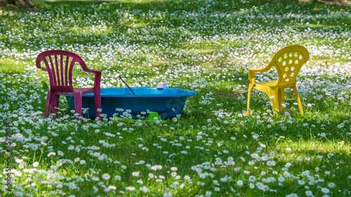 blue baby bath, red and yellow plastic chair in a green meadow