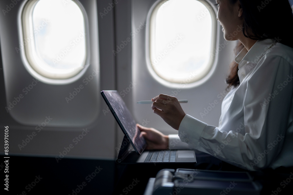 A woman is sitting on a plane with a laptop and a pen A woman is sitting on a plane with a laptop and a pen
