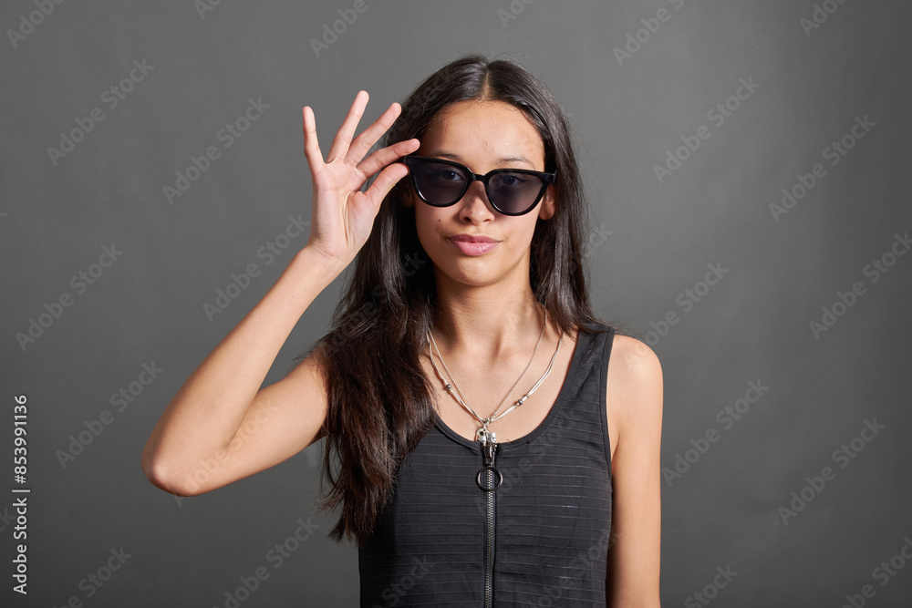 Studio photograph of a teenage girl with sunglasses. She is holding the glasses with her hand. She has a nice smile, latina girl. Studio photograph of a teenage girl with sunglasses. She is holding the glasses with her hand. She has a nice smile, latina girl.
