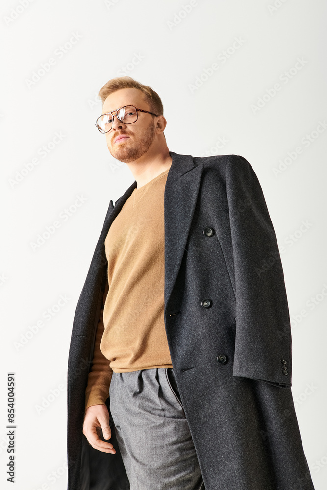 Fototapeta premium Handsome man in stylish long coat and glasses posing confidently.