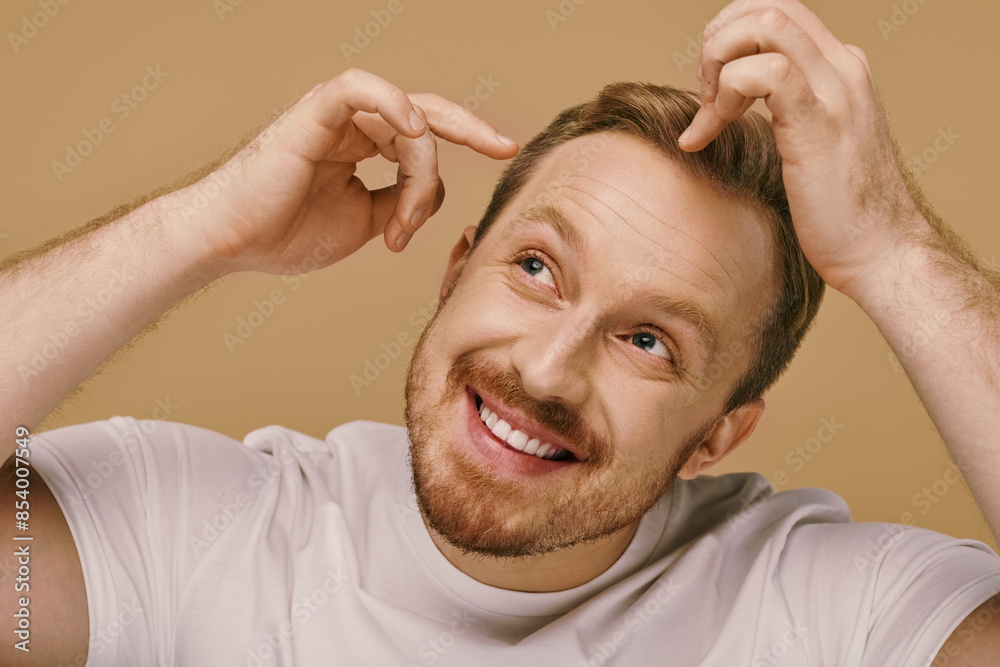 Obraz premium A man with a goatee smiles, holding his hair stylishly.