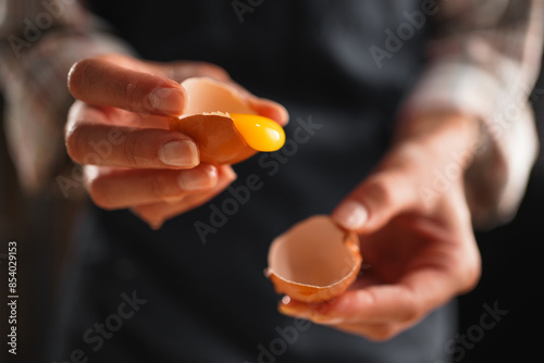 Tableau sur toile Female baker's hands cracking an egg with yolk dripping out, preparing for baking