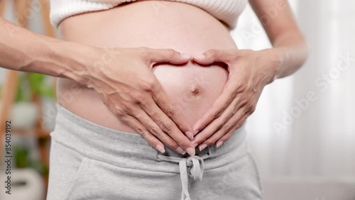 Wallpaper Mural Pregnant woman standing, hands forming heart shape on belly, Emphasizing love and connection with unborn baby, promoting healthy pregnancy, in cozy home setting. Torontodigital.ca