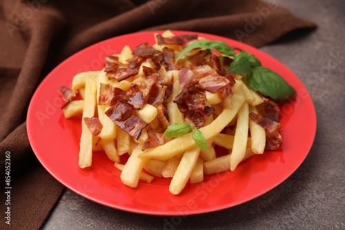 Delicious French fries with slices of bacon and basil on brown background, closeup