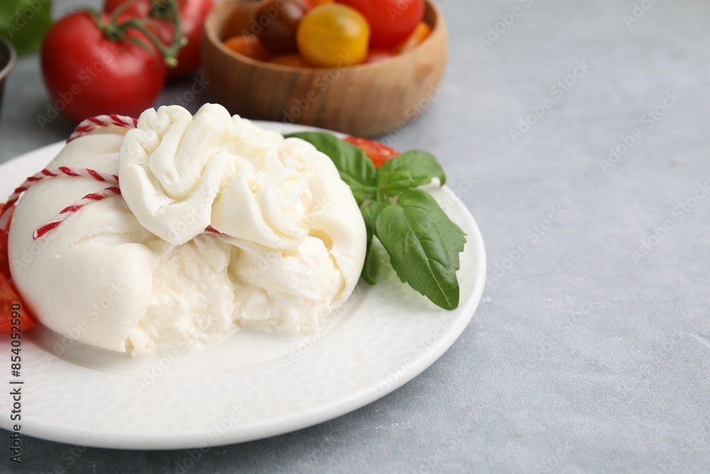 Delicious fresh burrata cheese with basil leaves on grey table, space for text Delicious fresh burrata cheese with basil leaves on grey table, space for text