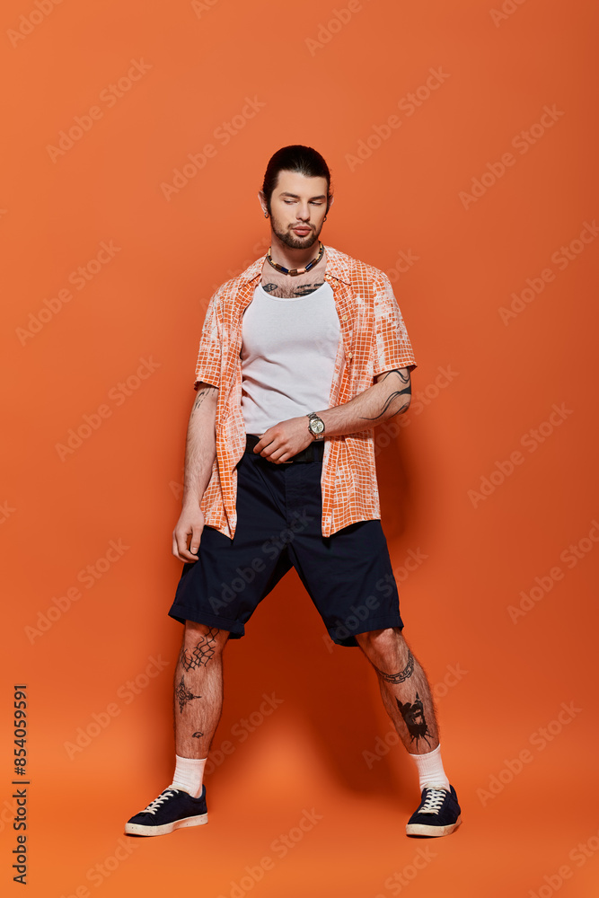 Handsome caucasian man in trendy attire standing confidently in front of a bright orange wall. Handsome caucasian man in trendy attire standing confidently in front of a bright orange wall.