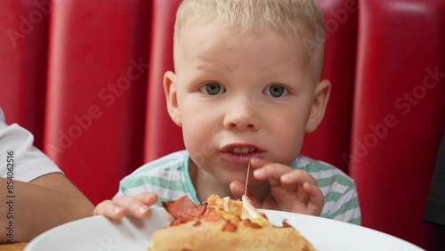 Boy eating pizza in a cafe against a red couch. Close-up of one child enjoying a large pizza. 