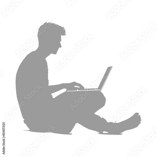 Silhouette of barefoot young man, cross-legged, intently typing on a laptop against white backdrop.