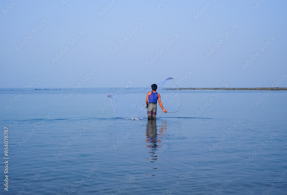 South asian young man throwing fishing net in sea water South asian young man throwing fishing net in sea water