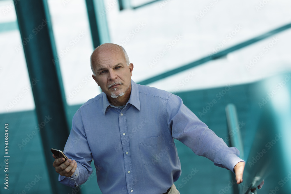 Fototapeta premium Senior businessman using smartphone app walking up stairs