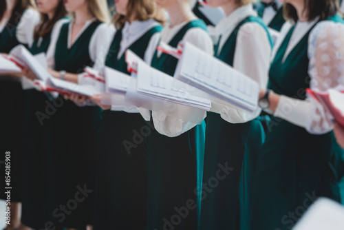 Church choir concert in cathedral, choral artists singing, group of European boys and girls singing in a chorus, students and choristers in white and green uniform performing on stage with conductor photo