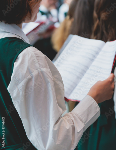 Church choir concert in cathedral, choral artists singing, group of European boys and girls singing in a chorus, students and choristers in white and green uniform performing on stage with conductor