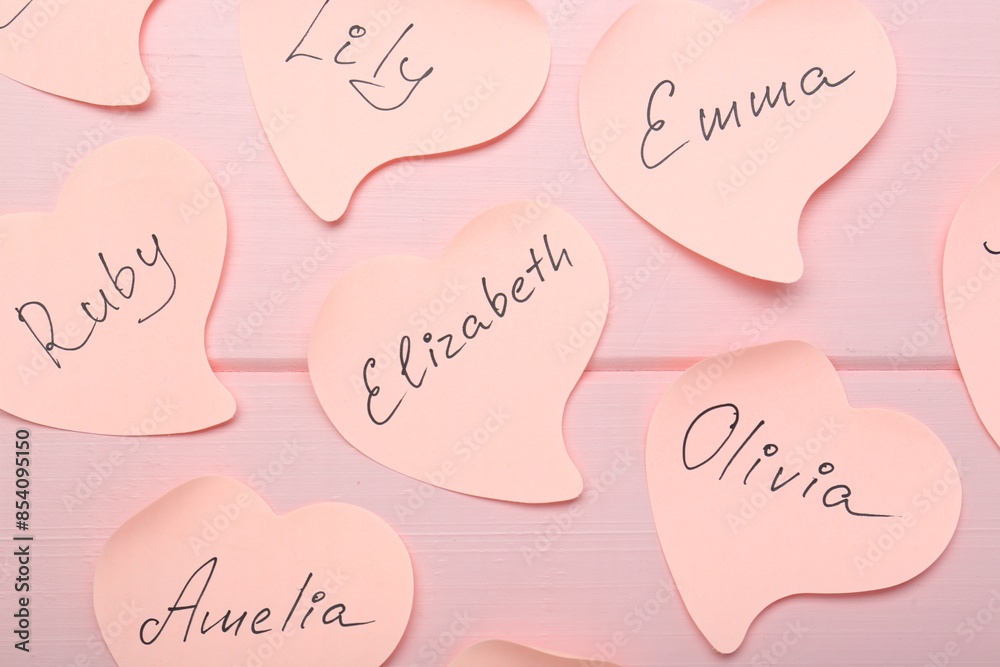 Paper stickers with different names on pink wooden background, flat lay. Choosing baby's name Paper stickers with different names on pink wooden background, flat lay. Choosing baby's name