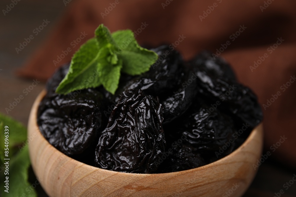 Tasty dried plums (prunes) and mint leaves in wooden bowl, closeup Tasty dried plums (prunes) and mint leaves in wooden bowl, closeup
