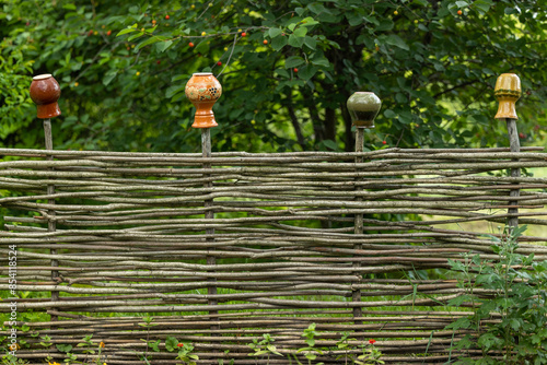 Wicker fence with clay jugs on the rods in the garden