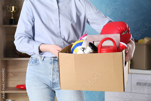 Woman holding box of unwanted stuff indoors, closeup photo