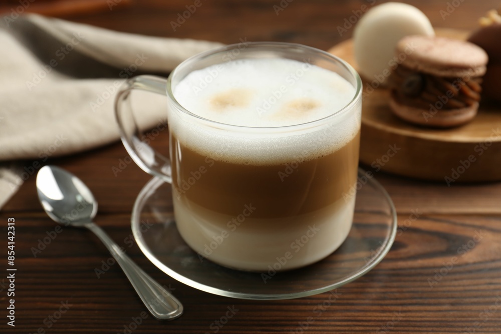 Aromatic coffee in cup, spoon and macarons on wooden table, closeup Aromatic coffee in cup, spoon and macarons on wooden table, closeup