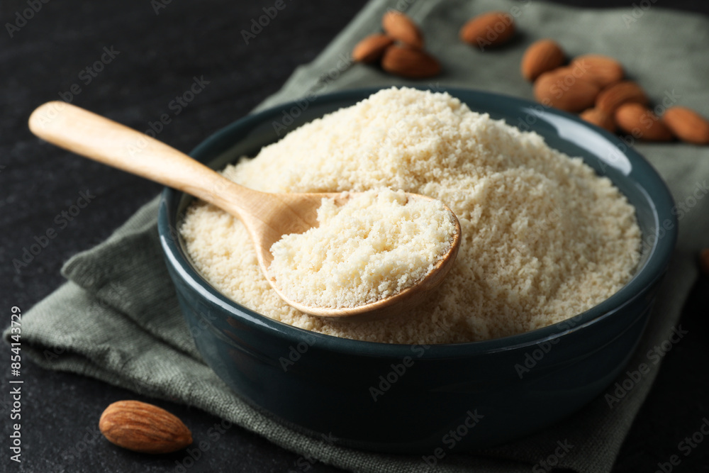 Fresh almond flour in bowl and spoon on dark textured table, closeup Fresh almond flour in bowl and spoon on dark textured table, closeup