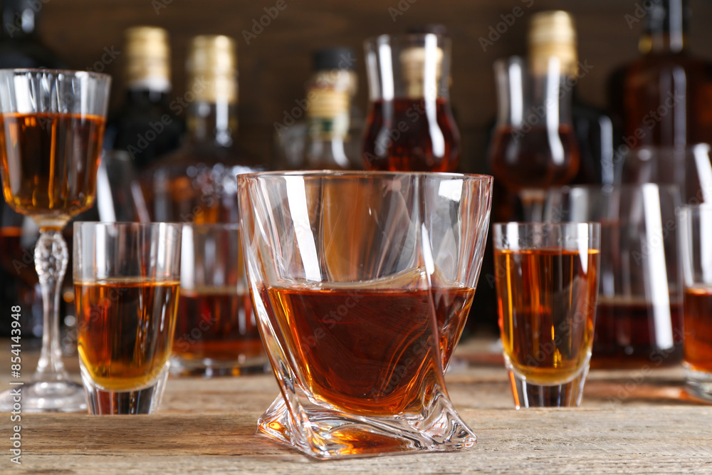 Different delicious liqueurs in glasses and bottles on wooden table Different delicious liqueurs in glasses and bottles on wooden table