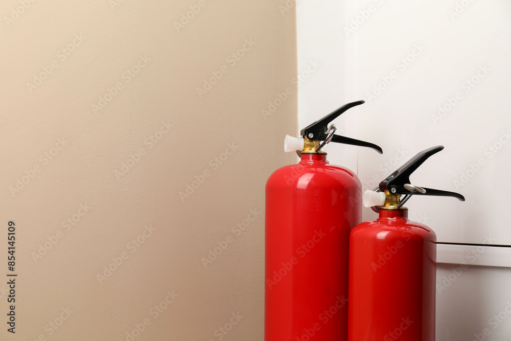 Obraz premium Two fire extinguishers near beige wall indoors, space for text