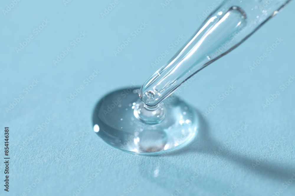 Glass pipette and transparent liquid on light blue background, closeup Glass pipette and transparent liquid on light blue background, closeup