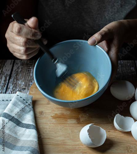 Concept of taking or grabbing food with hands, feminine Mexican hands. Scrambled eggs in a blue bowl with a fork on a wooden cutting board in a dark mood chiaroscuro style photo vertical image