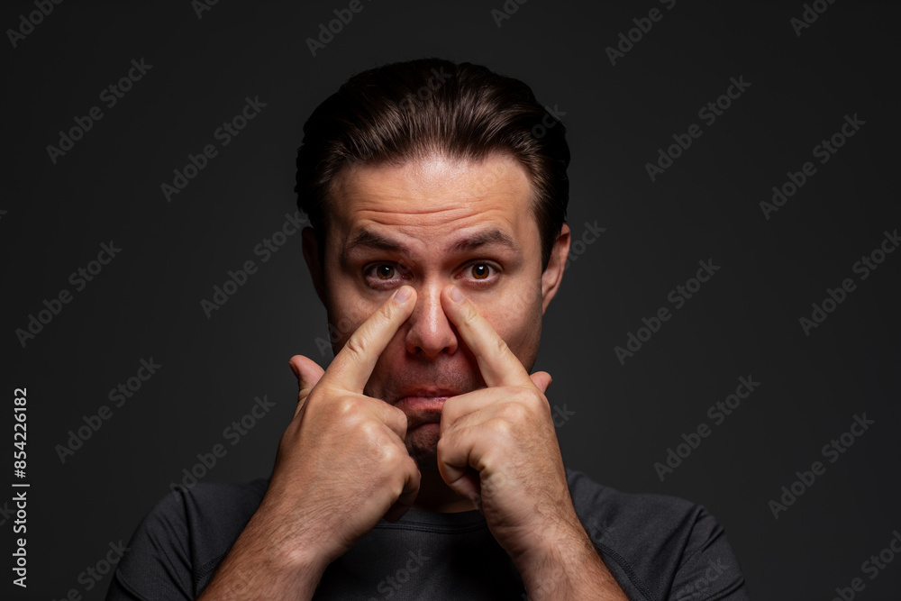 Man scratching his nose, portrait on dark background