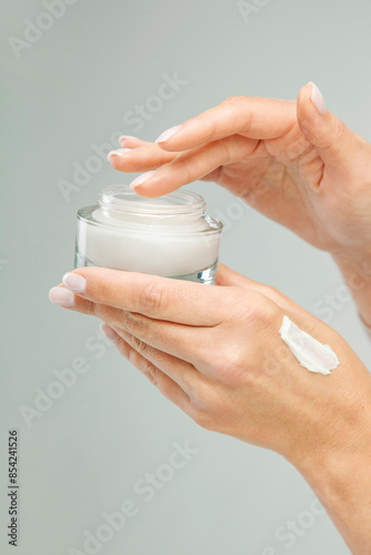 Female hand scooping cream from a glass jar. Woman's hands showing holding a glass container. Cosmetic product branding mockup. Daily skincare and face care routine. Smear of cream. Mock up, template