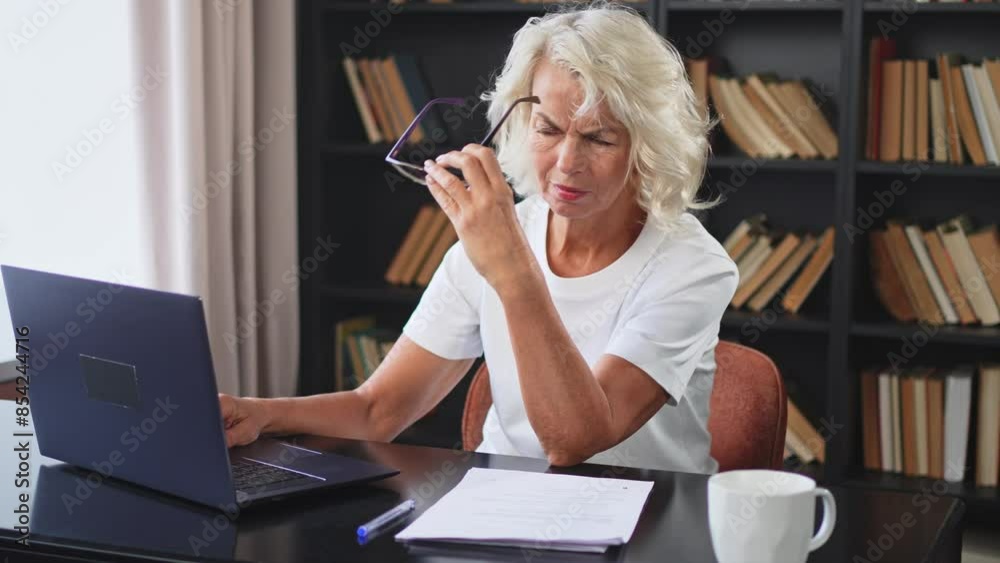 Confident stylish middle aged senior woman using laptop at workplace. Older mature lady businesswoman sitting at office table with laptop and paper document. Boss leader teacher professional worker