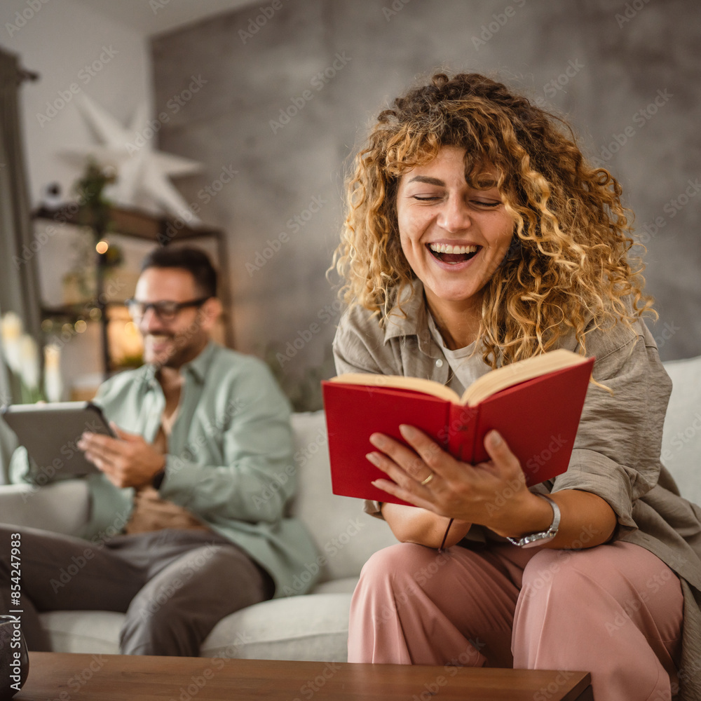 Girlfriend read a book while his boyfriend use tablet at home Girlfriend read a book while his boyfriend use tablet at home